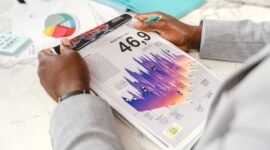 Seorang eksekutif bisnis sedang menganalisis grafik kinerja keuangan dalam laporan tahunan, yang menggambarkan upaya memahami arah dan strategi perusahaan. Gambar ini merepresentasikan pentingnya membaca data secara cermat untuk mengidentifikasi kisah di balik angka-angka perusahaan.