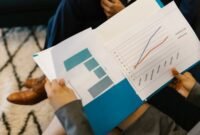 Beberapa profesional sedang menganalisis grafik dan data dari laporan tahunan perusahaan, mencerminkan proses mendalam dalam memahami kinerja dan merencanakan strategi bisnis. Interaksi tersebut menunjukkan pentingnya diskusi dan kolaborasi untuk menginterpretasi informasi kompleks yang disajikan dalam dokumen tersebut.