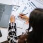 Seorang profesional tengah menganalisis detail laporan tahunan perusahaan yang terhampar di meja, menunjukkan kompleksitas dan kekayaan informasi yang terkandung dalam dokumen penting tersebut. Laporan ini bukan sekadar kumpulan angka, melainkan cerminan strategi dan perjalanan bisnis selama setahun penuh.
