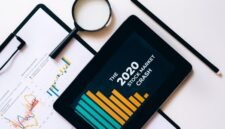 Ilustrasi tumpukan laporan tahunan dengan laptop yang menampilkan grafik data, mencerminkan perpaduan antara format tradisional dan digital dalam penyajian informasi perusahaan. Desain modern pada laporan menunjukkan komitmen perusahaan terhadap transparansi dan komunikasi yang efektif kepada para pemangku kepentingan.