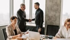 Sebuah adegan menunjukkan jabat tangan erat antara pebisnis di sebuah kantor modern yang mencerminkan kolaborasi dan kesepakatan penting terkait investasi atau penambahan modal. Latar belakang kota yang sibuk melambangkan dinamika ekonomi dan peluang pertumbuhan yang akan dibentuk dari keputusan strategis ini.