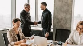 Sebuah adegan menunjukkan jabat tangan erat antara pebisnis di sebuah kantor modern yang mencerminkan kolaborasi dan kesepakatan penting terkait investasi atau penambahan modal. Latar belakang kota yang sibuk melambangkan dinamika ekonomi dan peluang pertumbuhan yang akan dibentuk dari keputusan strategis ini.