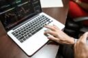 Grafik kompleks yang menunjukkan fluktuasi harga saham di bursa, dengan tangan seseorang sedang menganalisis data keuangan pada layar, menggambarkan upaya memahami valuasi saham di tengah dinamika pasar.