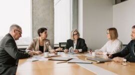 Dewan direksi dan komisaris berdiskusi serius, menunjukkan komitmen terhadap prinsip tata kelola perusahaan yang baik demi keberlanjutan bisnis dan kepercayaan investor. Meja rapat yang tertata rapi melambangkan struktur organisasi yang teratur dan pengambilan keputusan yang terencana.